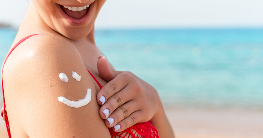 Spalla di ragazza al mare con smiley fatto con crema solare